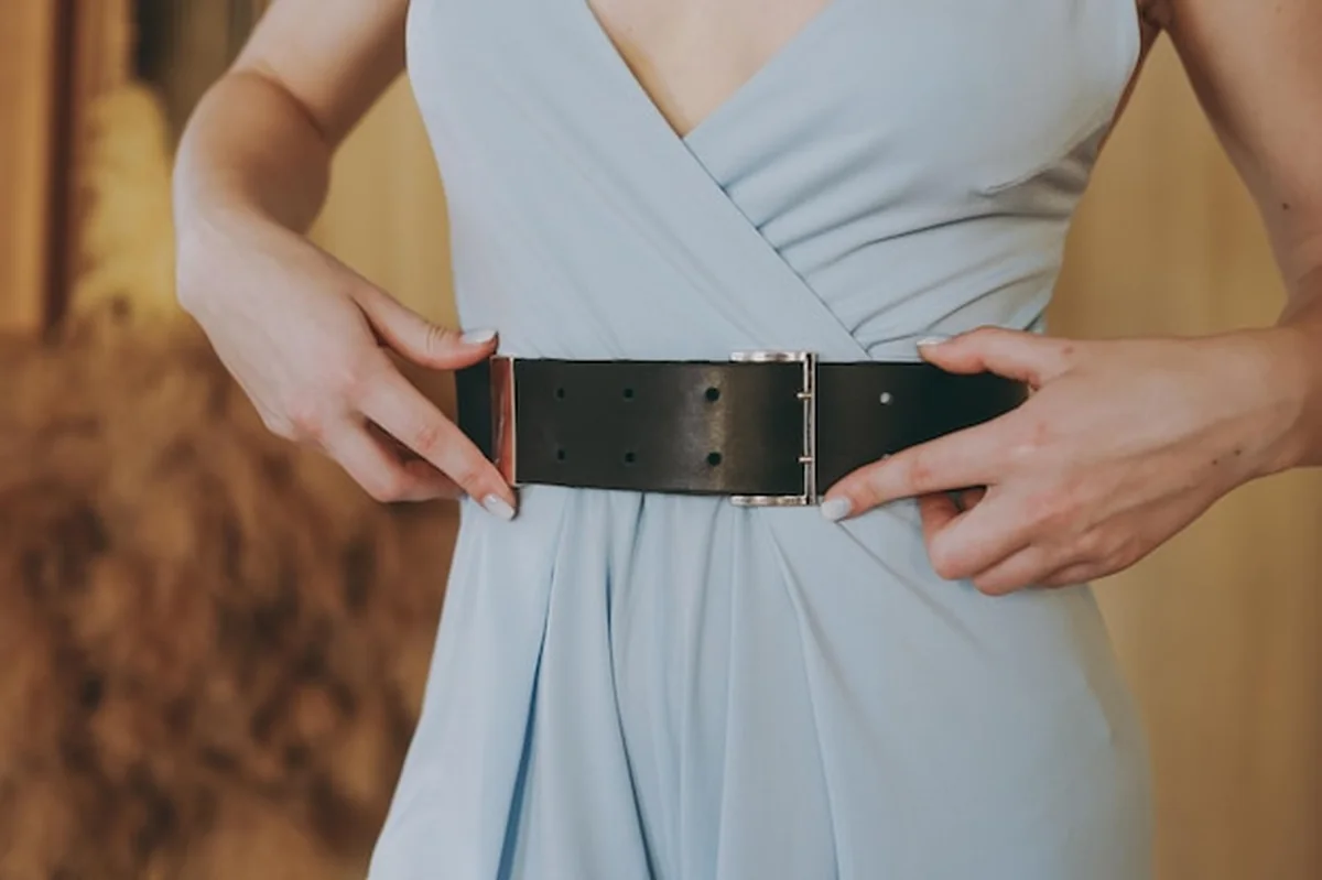 Młoda dziewczyna w niebieskiej sukience przymierza skórzany pasek