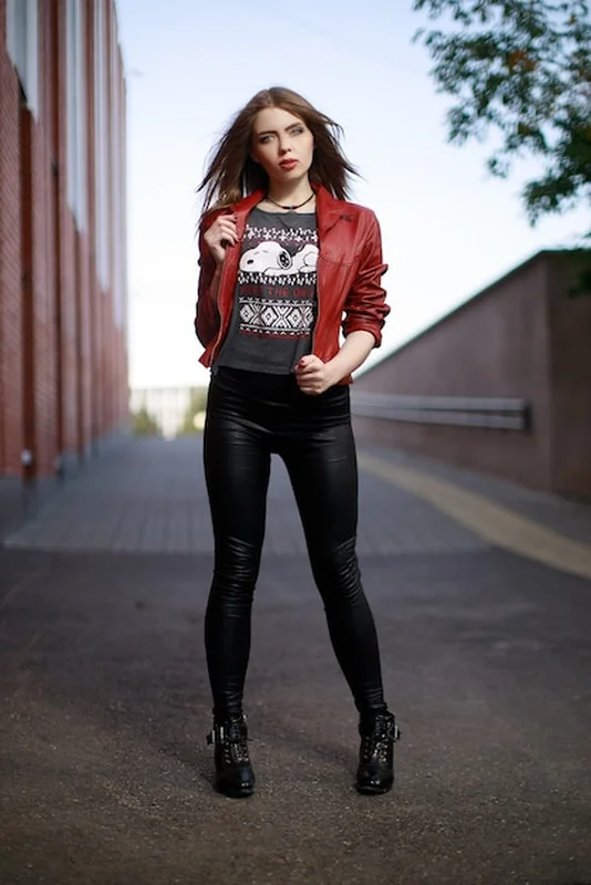 Młoda kobieta w czerwonej skórzanej kurtce i czarnych legginsach w mieście w ciągu dnia