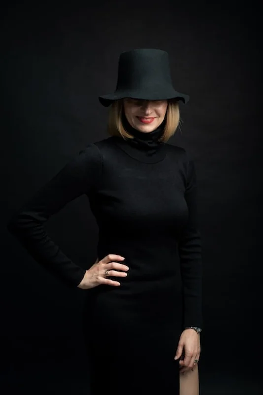 Blond kobieta w czarnej sukience i kapeluszu na ciemnym tle