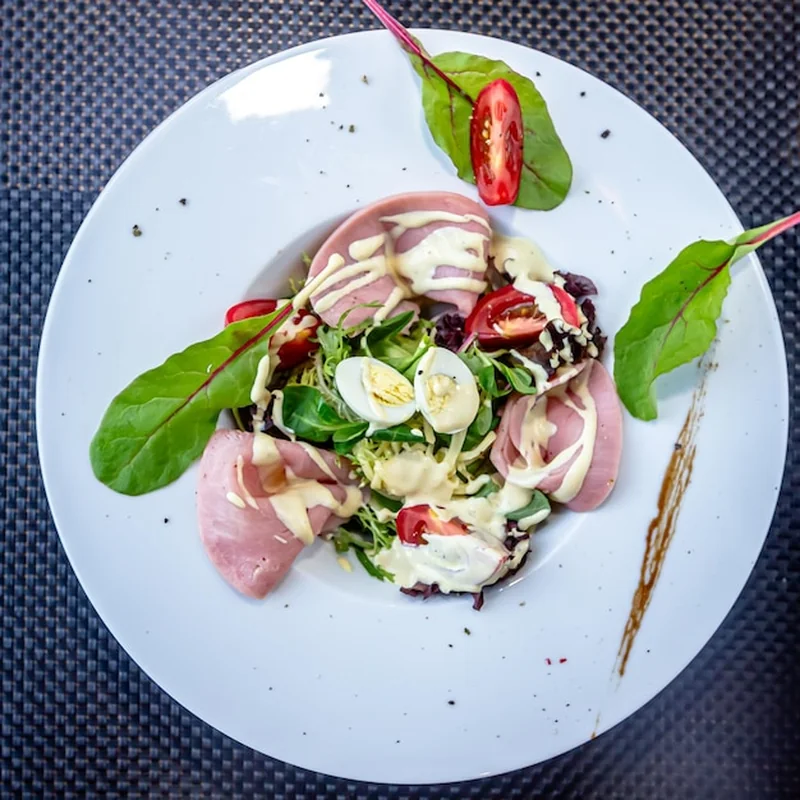 Sałatka z szynką, rukolą i jajkami przepiórki na białym talerzu