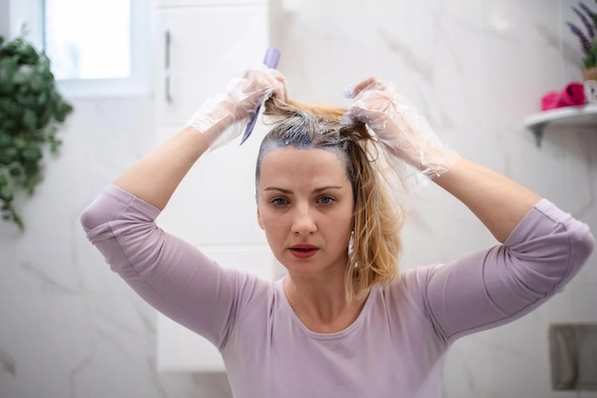 Kobieta farbuje włosy w domu za pomocą szczotki i plastikowych rękawiczek