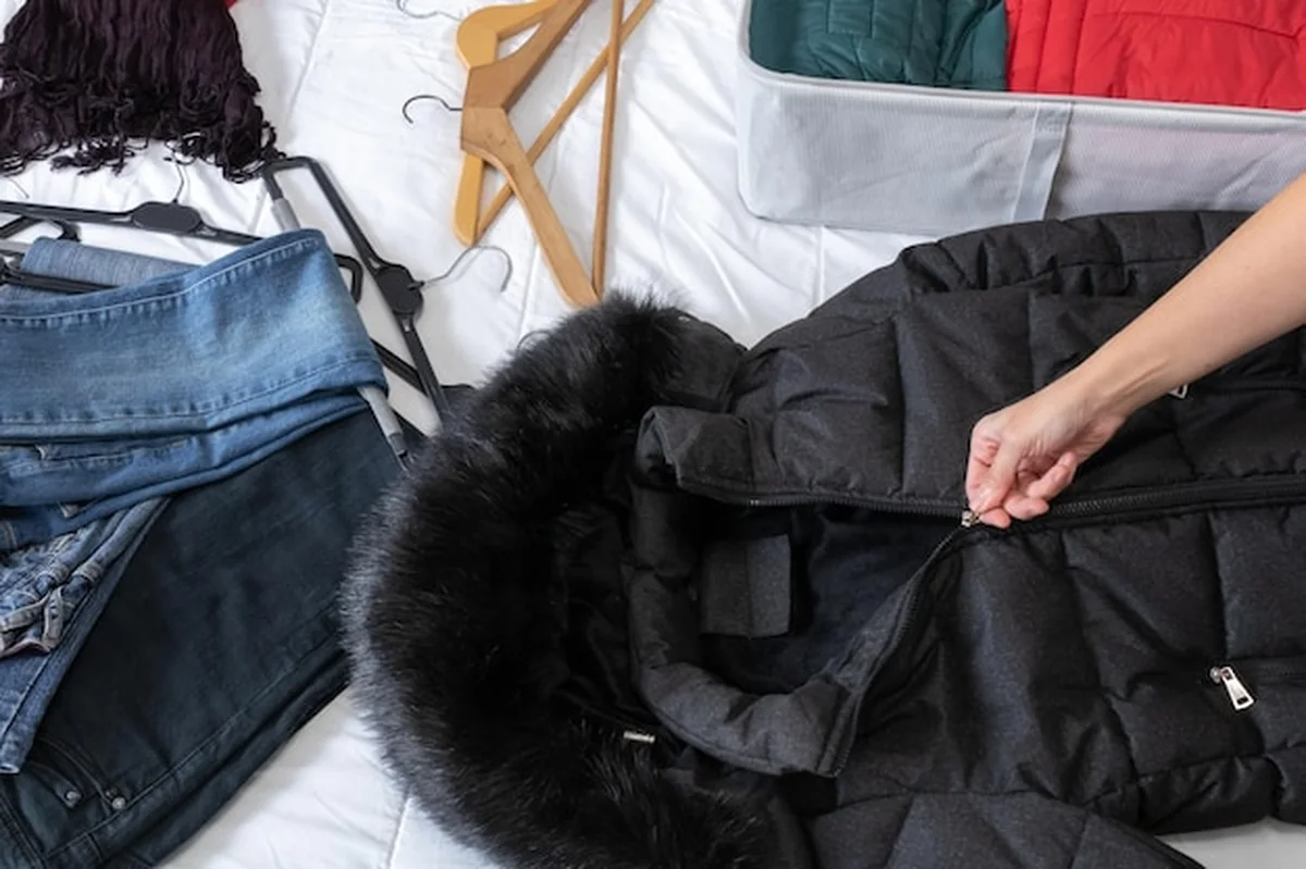 Ręka kobiety zamykająca zamek czarnego płaszcza na łóżku