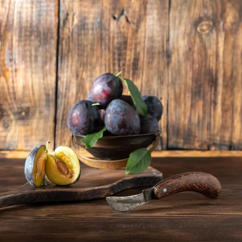 Miska z owocami śliwek na drewnianym stole pod światłem okna