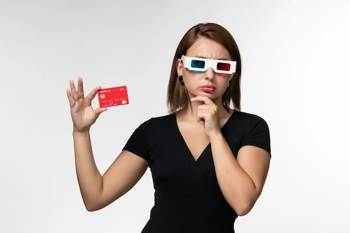 Młoda kobieta trzyma kartę bankową w okularach przeciwsłonecznych na białej powierzchni