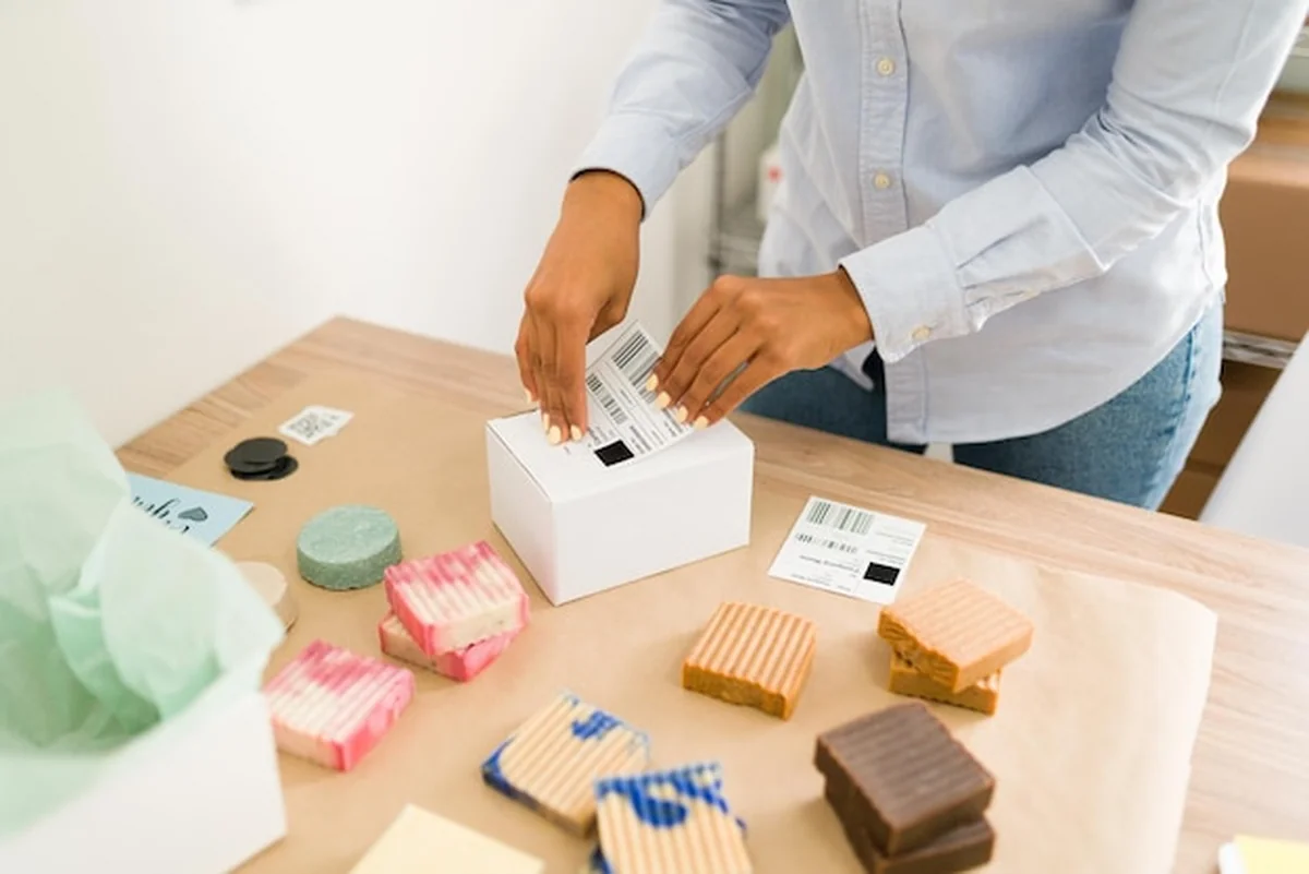 Kobiece dłonie nakładają etykietę na opakowanie z produktami pielęgnacyjnymi