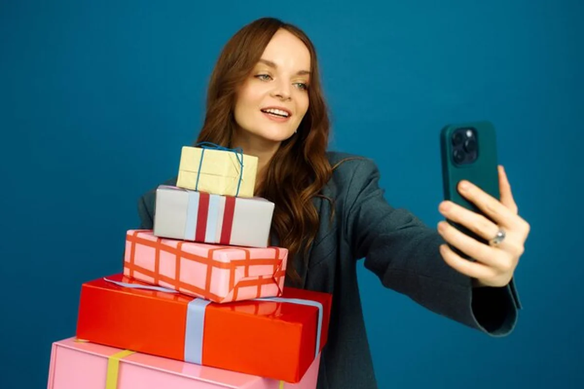 Kobieta uśmiecha się, robiąc selfie z kolorowymi prezentami podczas noworocznej celebracji w pomieszczeniu