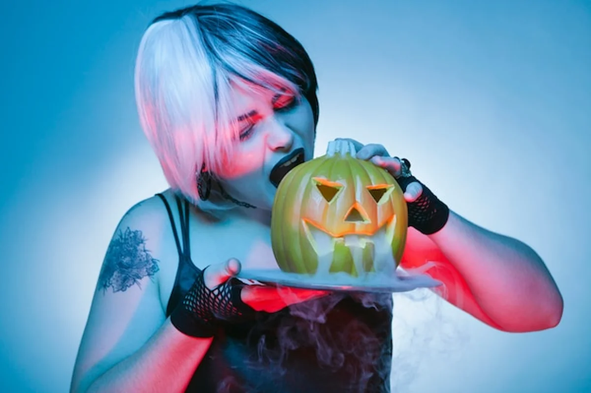 Goth kobieta jedząca kęs palonej dyni w Halloween