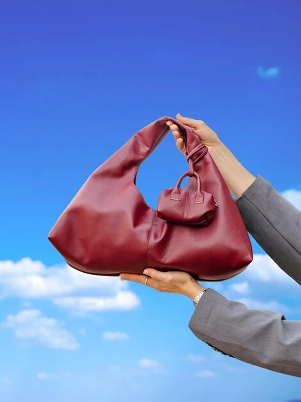 Kobieta trzymająca stylową czerwoną torebkę i małą portmonetkę przed niebieskim niebem