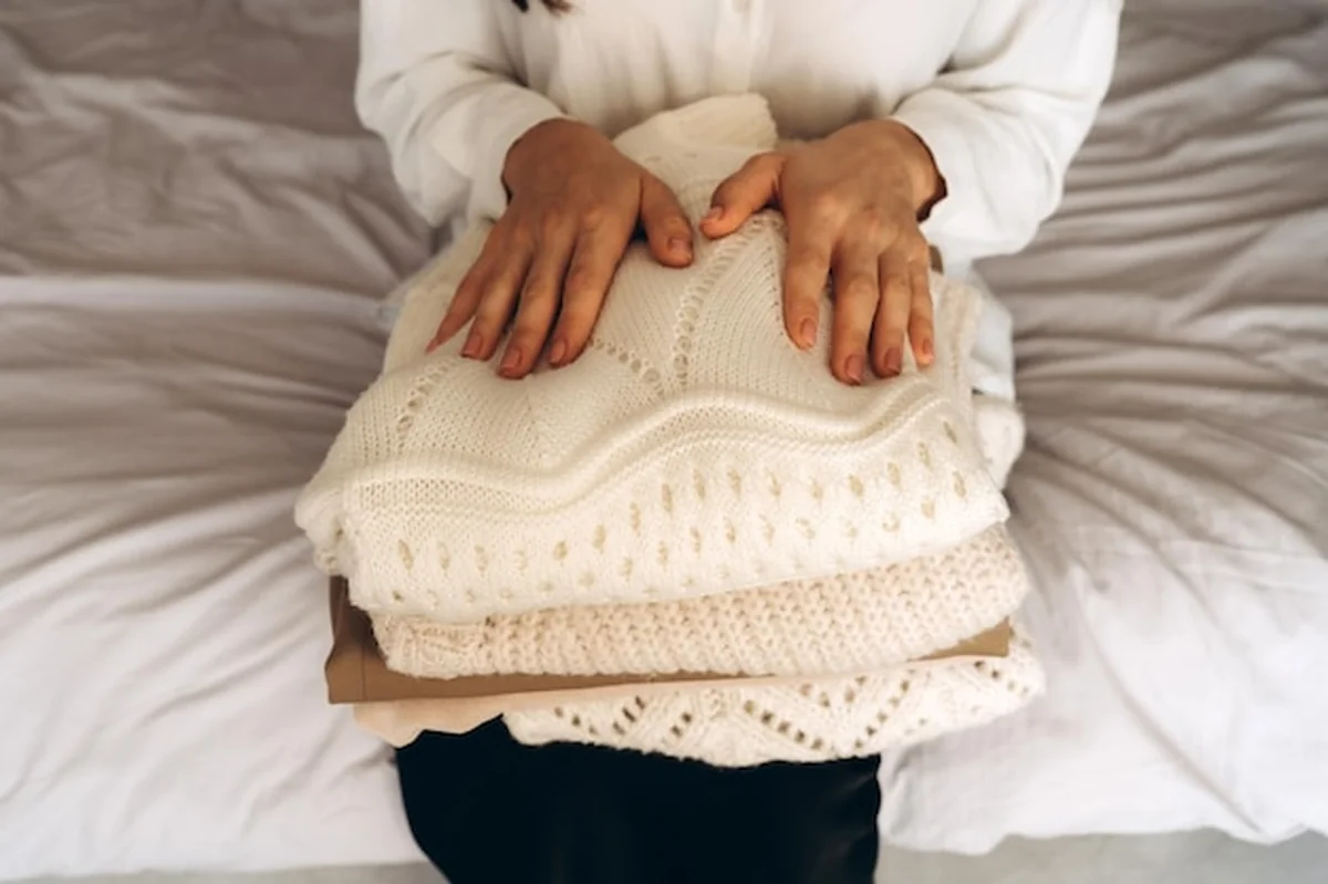 Kobieta trzymająca złożone sweterki z dzianiny