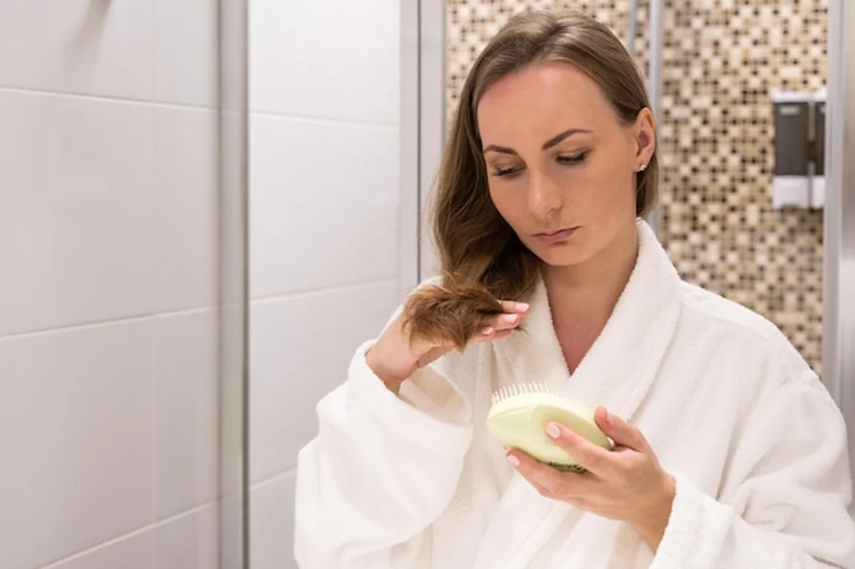 Młoda kobieta w białym szlafroku szczotkuje długie włosy patrząc w lustro