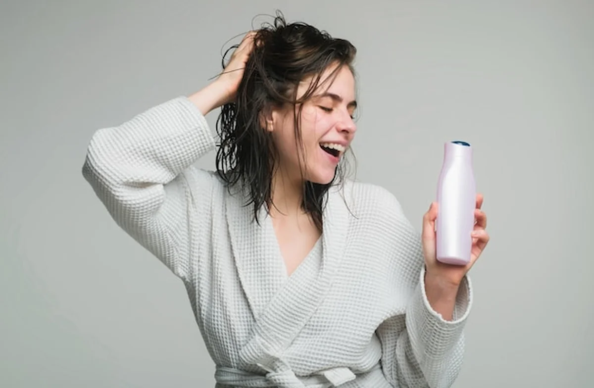 Młoda kobieta dotykająca włosów trzyma butelkę szamponu i odżywki